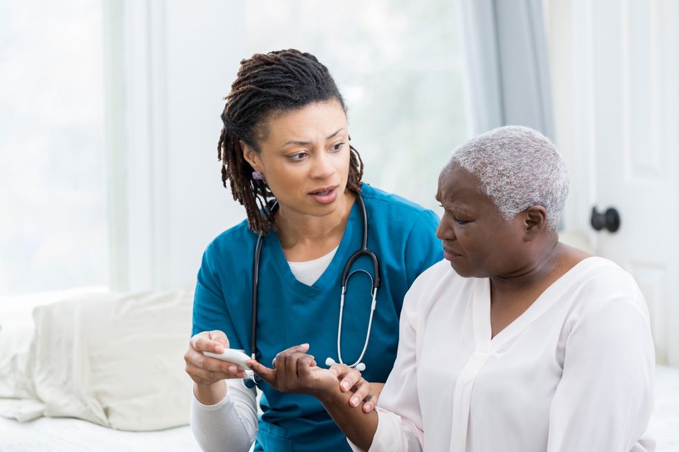 Concerned African American nurse uses glaucometer to check a female patient's blood sugar level