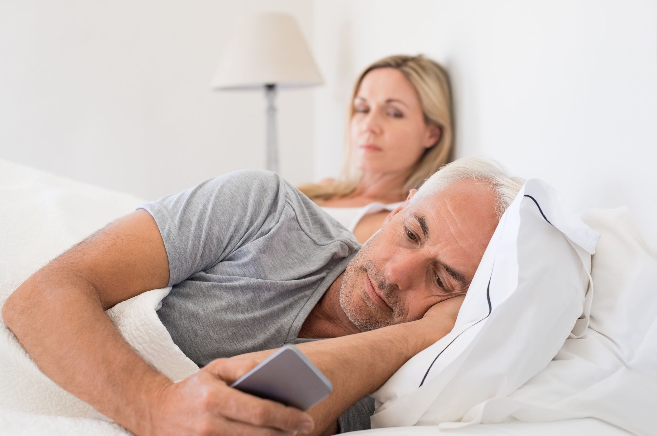 Senior couple in bed while wife is angry as husband using smartphone