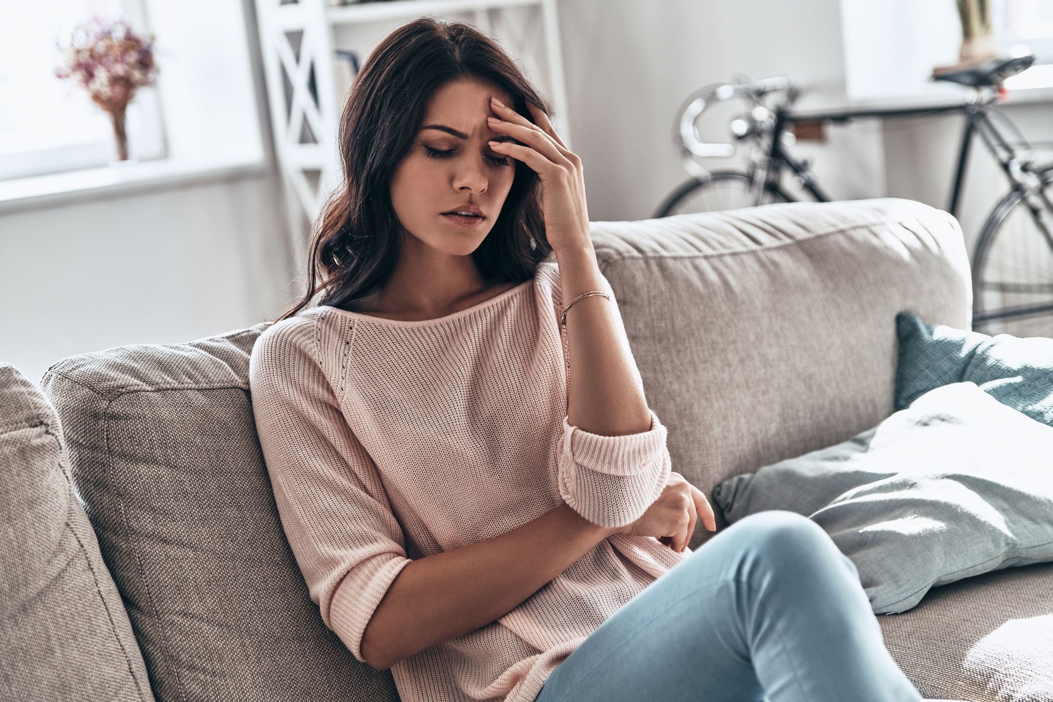 stressed out young woman suffering from the headache while sitting on the sofa at home