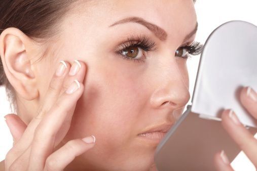 Woman With Alopecia looking at her face closely in a pocket mirror