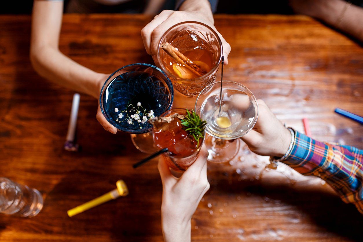 friends clinking by glasses with various alcoholic cocktails at table