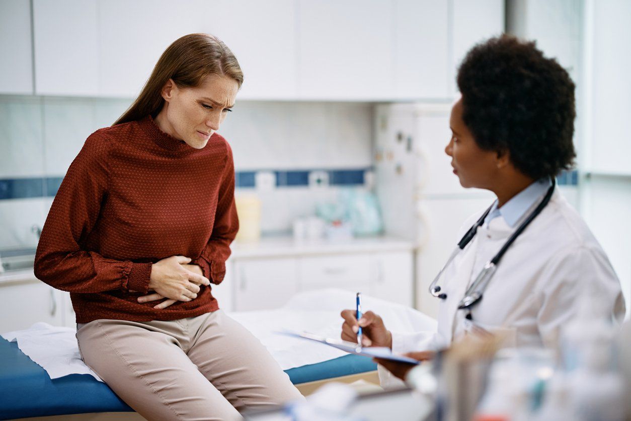 Female patient holding her abdomen in pain while talking to her doctor at medica clinic.