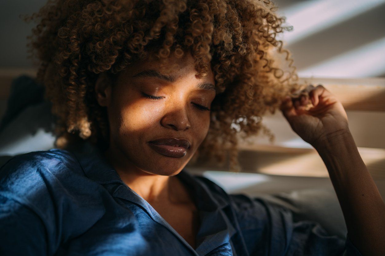 African American woman in pajamas resting in her bed at home.