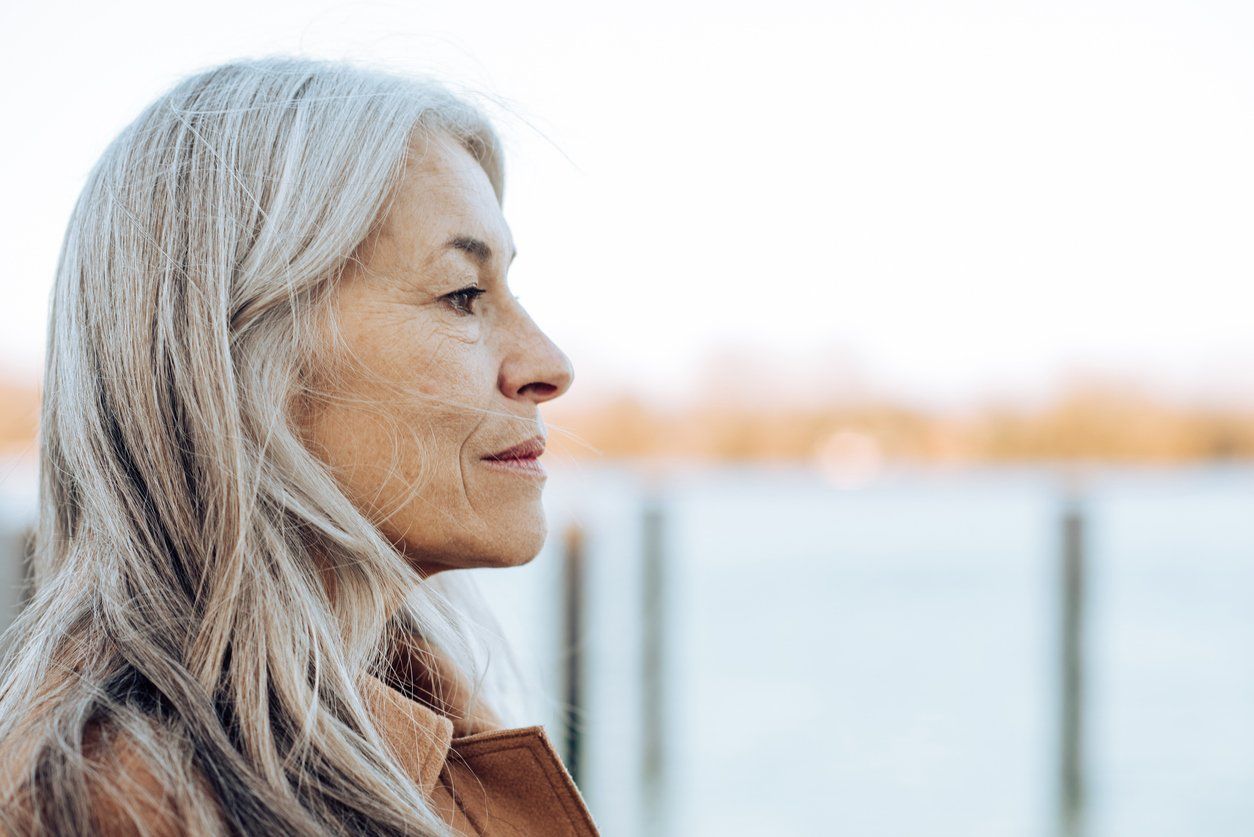 thoughtful mature woman standing on the beach and looking at the distance.