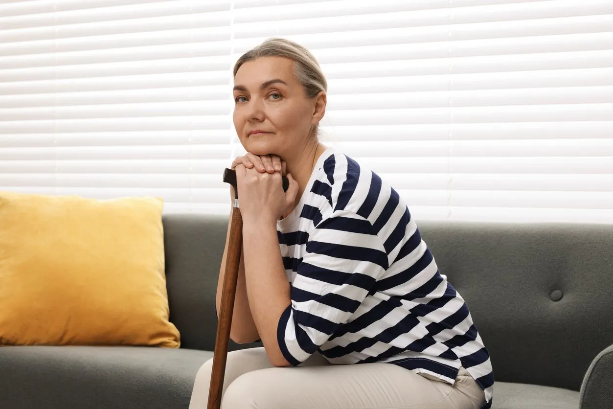 Senior woman with walking cane sitting on sofa at home