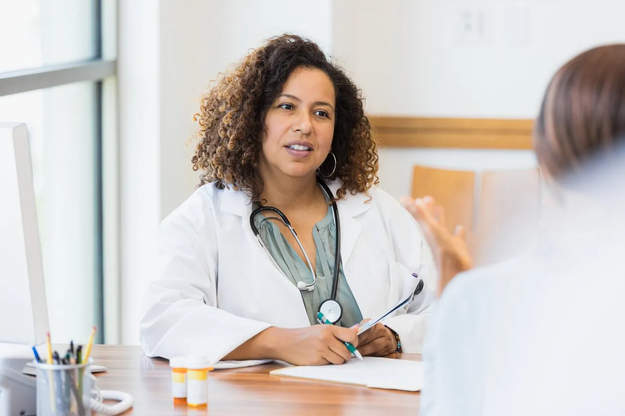 female doctor sits at desk while listening to patient