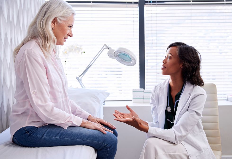 Mature Woman In Consultation With Female Doctor Sitting On Examination Couch