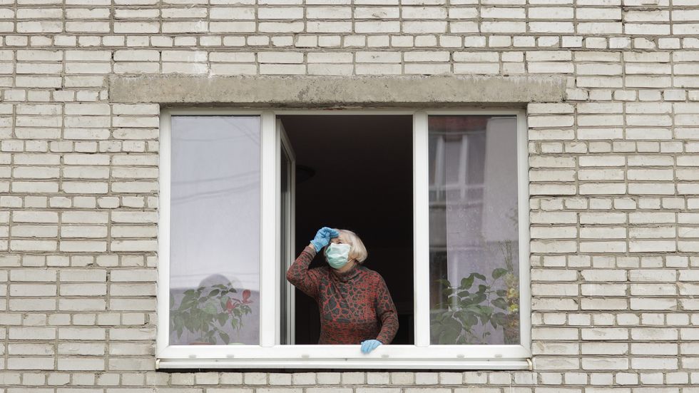 Old woman stay at window in protection mask