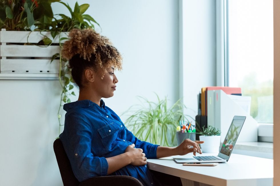 Pregnant businesswoman with hand on stomach working at desk