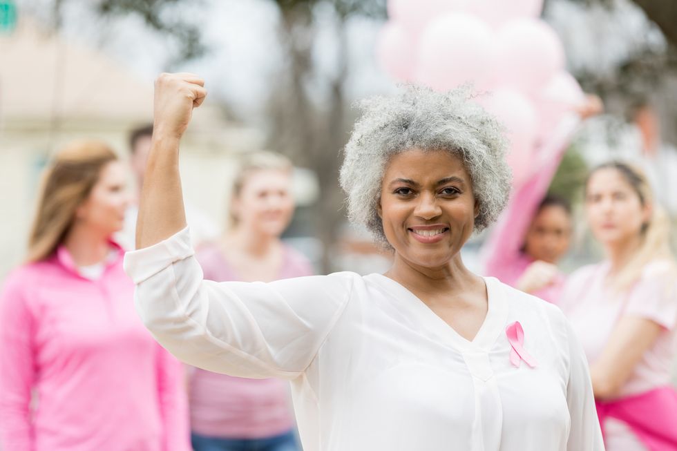 senior breast cancer survivor flexes her muscles during breast cancer awareness race.