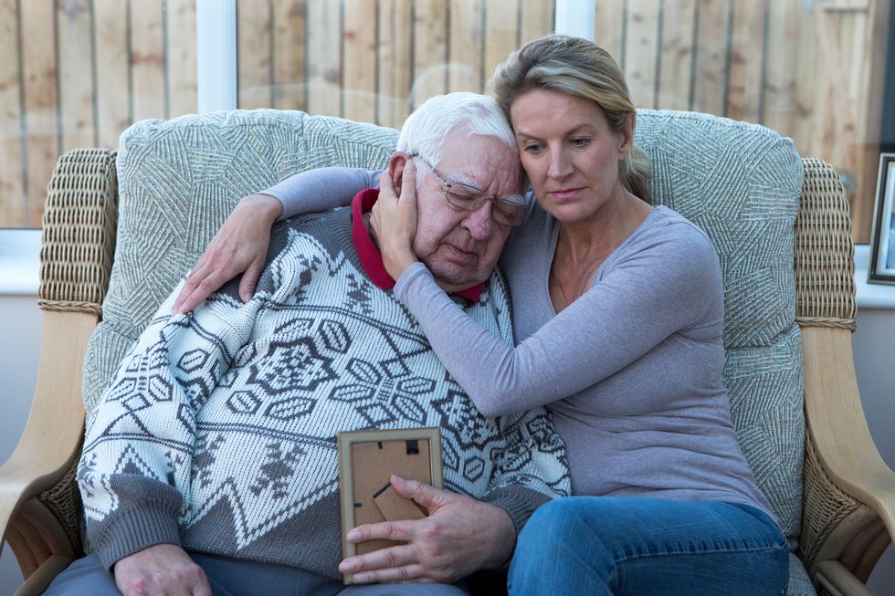 senior man sitting on the sofa with his daughter, looking at a photograph