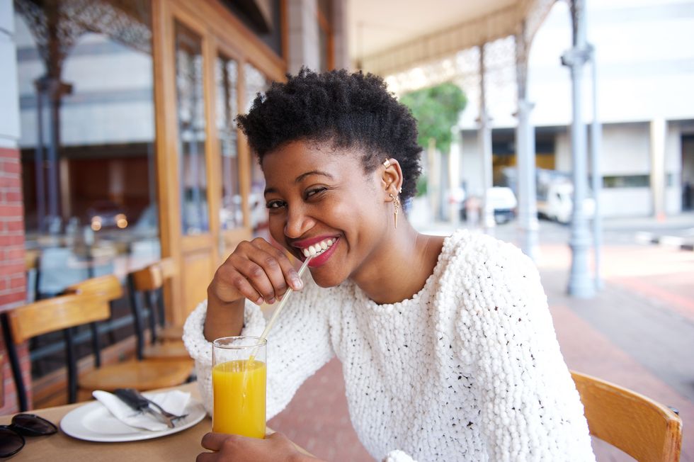 smiling black girl drinking orange juice at outdoor cafe