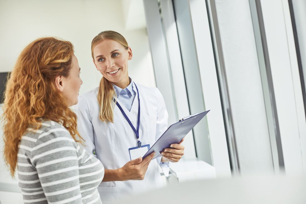 smiling gynecologist standing with red-haired woman in medical office