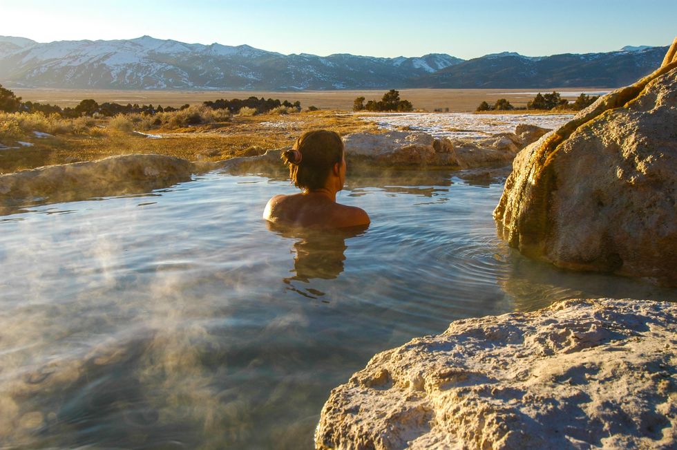 Woman enjoys view of Sierra Nevada Mountains while soaking in hot spring.