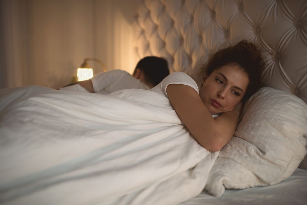 woman with a sad expression laying in bed next to partner